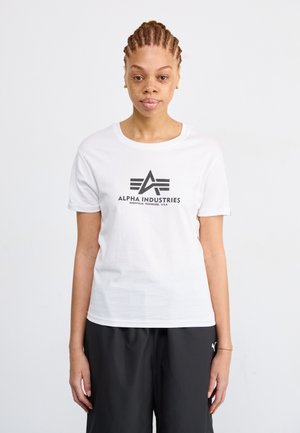 T-shirt en coton blanc à manches courtes avec un logo graphique noir "ALPHA INDUSTRIES" et des lignes horizontales en dessous. Design simple à col rond.