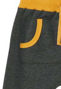 Grijze sweatpants met een geribbelde gele tailleband en zakafwerking. Voorzien van een trekkoord en zachte, gestructureerde stof.
