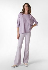 Ljuslila oversized skjorta med trekvartslånga ärmar, ihop med matchande utsvängda byxor och beige skor, mot en vit bakgrund.