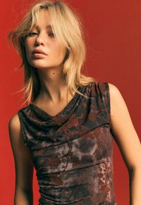 Hnedo-sivá šatka bez rukávov s kvetinovým vzorom a drapovaným výstrihom, s textúrovanou tkaninou a zhromaždením detailu. Pozadie je červené.