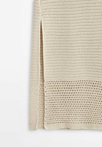 Tissu tricoté beige avec une fente sur le côté et un motif ajouré texturé au bord inférieur.