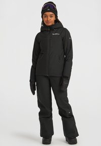 Zwarte skijas met een rits aan de voorkant, capuchon en logo. Gecombineerd met bijpassende zwarte skibroeken en handschoenen, geschikt voor koud weer.
