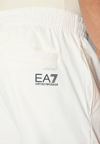 Bela športna hlače z elastičnim pasom, zadnjim žepom in logotipom "EA7 EMPORIO ARMANI". Gladka, lahka tkanina.