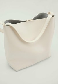 Romige witte schoudertas van glad materiaal, met een brede opening en een enkele schouderriem. Het interieur heeft een grijze voering.