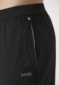 Black athletic shorts made from soft fabric, featuring a side pocket with gray trim and a small, embroidered logo on the front.