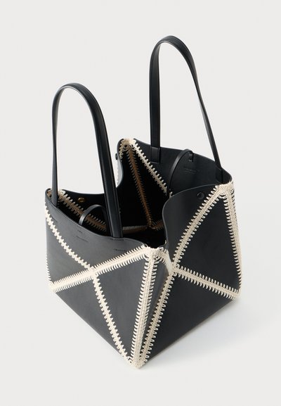 Black leather tote bag with a geometric design, featuring contrast stitching in white. The shape is angular with two sturdy straps.
