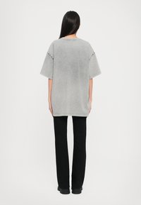 Grijze oversized t-shirt met een ronde hals, korte mouwen en subtiele stiksels, gecombineerd met zwarte rechttoe-rechtaan broeken.