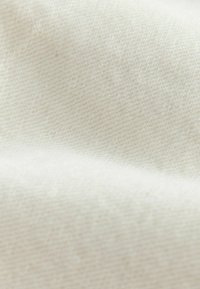 Közelkép lágy, törtfehér anyagról, finom szövött textúrával és enyhe redőkkel.