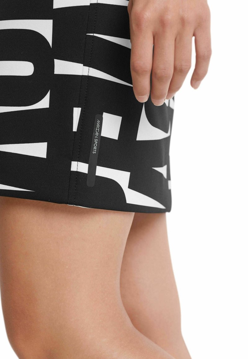 Schwarzer sportlicher Rock mit großem weißen Textdruck, elastischem Stoff und einem kleinen Etikett mit der Aufschrift "MARCONI SPORTS" nahe dem Saum als Markenzeichen.