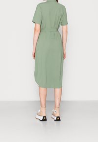 Grön klänning med korta ärmar och bälte i midjan, som faller vid vaden. Matchad med beige ankelstövlar med svart klack och stjärndetalj.