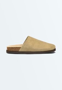 Mule beige en daim à enfiler avec semelle intérieure en liège et semelle extérieure noire texturée, présenté de profil sur fond blanc.