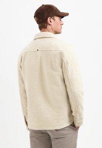 Beige fleece jack met een textuurafwerking, voorzien van een klassieke kraag, knoopdetail op de rug en lange mouwen.