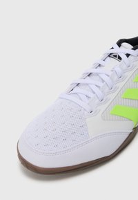 White sports shoe with mesh toe, white laces, neon green side stripes, and brown sole on a white background.