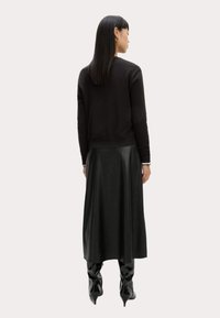 Un pull noir ajusté à manches longues associé à une jupe en cuir noir longueur sol. La tenue présente un design élégant et minimaliste.