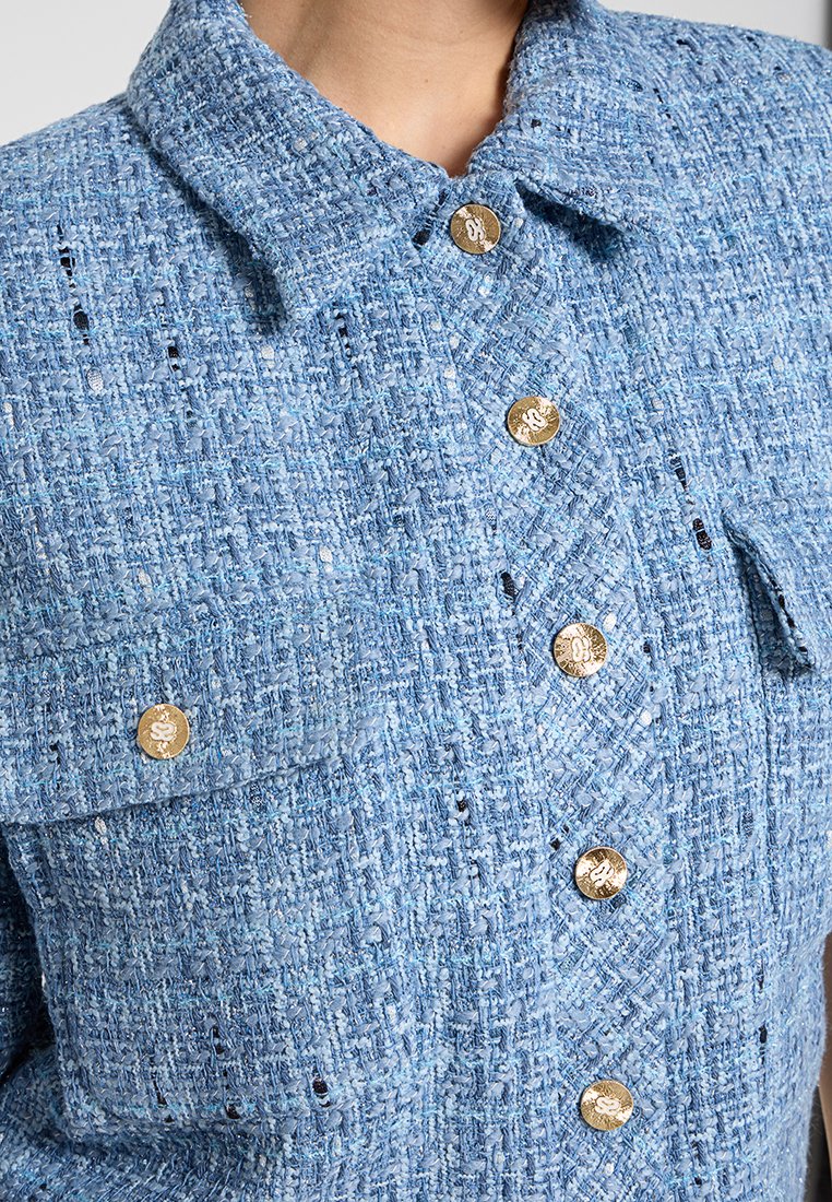 Hellblaues Tweed-Jackett mit Kragen, goldenen Knöpfen und einem strukturierten Muster. Enthält zwei vordere Taschen mit Klappen.