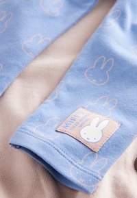 Blått tyg med Miffy-mönster, med en texturerad lapp. Mjukt, tunt material lager på en ljusbeige bakgrund.