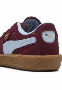 Sneaker in suede marrone con accenti blu e logo dorato. Presenta una suola in gomma texturizzata e cuciture bianche. Design con punta tonda.