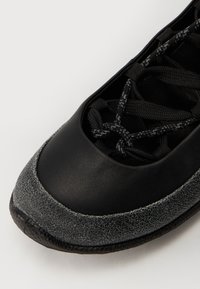 Svarte lærersneakers med en teksturert grå gummisåle. Har svarte snørebånd og en glatt overdel. Rund tå-design.