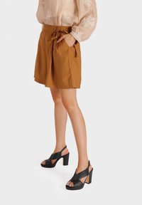 Pantaloni corti marroni con vita cintura, abbinati a sandali neri con tacco caratterizzati da un design a fascia incrociata e materiale testurizzato.