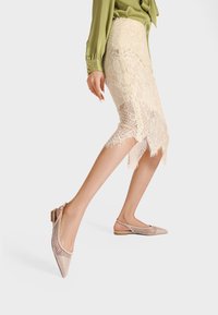 Ballerine escluse dalla punta affusolata in nude con design a rete, tacco piatto e texture contrastanti. La scarpa presenta una silhouette elegante e dettagli intagliati.