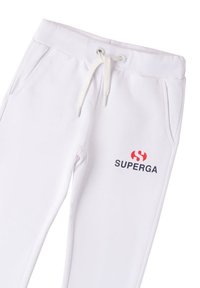 Pantalones de chándal blancos con cordón, con bolsillos laterales y un logo rojo y negro de "SUPERGA" en el muslo izquierdo.