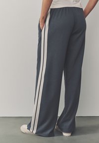 Tummansiniset leveälahkeiset housut valkoisilla sivuraitoja, pehmeästä kankaasta, taskuilla ja mukavalla joustavalla vyötärönauhalla.