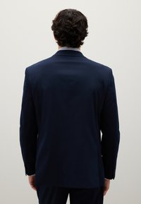 Giacca da abito blu marina, design a un petto, tessuto liscio e leggermente strutturato. La vista posteriore mostra una vestibilità su misura e una leggera struttura delle spalle.