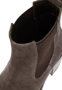 Bruine suède enkellaars met ribbel-elastische zijkanten en een slanke hak. Het interieur heeft een gladde zwarte voering.