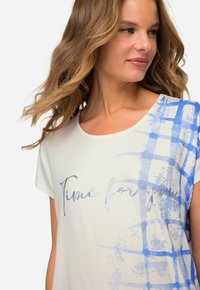 Lysfarvet T-shirt med korte ærmer, som har blå abstrakte penselstræk mønstre og teksten "Tid til dig" i en skriftskrift.