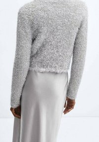 Maglione di maglia argentata e pelosa con maniche lunghe, di lunghezza cropped, abbinato a una gonna in satin grigio chiaro e liscia.