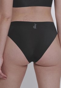 Slip bikini nero con aperture alte sulle gambe, design senza cuciture e texture liscia. Presenta un piccolo logo vicino alla vita.