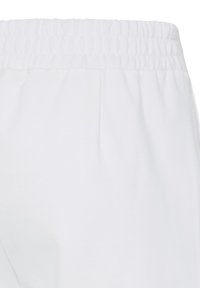 Gros plan sur une ceinture élastique de pantalon blanc uni, montrant la texture du tissu et les détails de la couture.