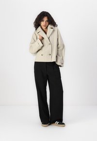 Beige double-breasted cropped jacket with wide lapels and rolled cuffs, paired with black wide-leg trousers and casual black sneakers.