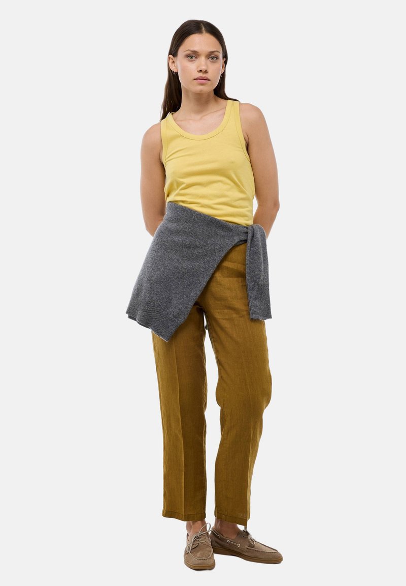 Débardeur jaune, écharpe tricotée grise autour de la taille, pantalon en lin beige et chaussures marron clair. Design simple avec une coupe décontractée et une palette de couleurs neutres.
