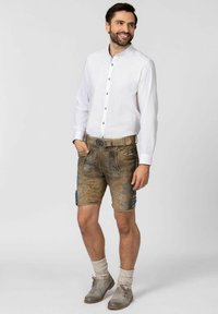 Weißes Langarmhemd mit Knöpfen, kombiniert mit braunen Ledershorts mit blauen Stickereien und einer dekorativen Gürtelschnalle.
