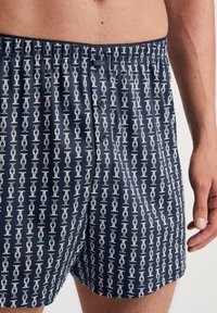 Navy blauwe katoenen boxers met een herhalend kettingpatroon in wit en groen. Elastische tailleband met knoopsluiting en subtiele logodetail.