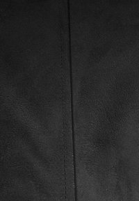 Matériau en cuir noir avec une couture centrale comportant des points détaillés courant verticalement au milieu.
