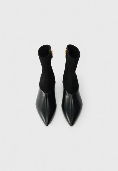 Czarne botki za kostkę z wąskim czubkiem, z gładką skórzaną przodem i miękkim materiałem na górze, ozdobione złotym zamkiem z tyłu.