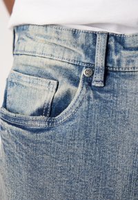 Light blue denim jeans with a faded finish, visible pocket stitching, and metal button accent. Features a classic five-pocket design.