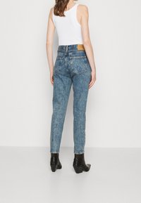 Světle modré džínové kalhoty s vysokým pasem, rovného střihu, dvěma zadními kapsami a koženou nášivkou na pase, doplněné černými botami na podpatku.