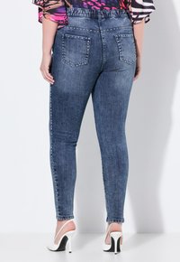 Chude jeansy w ciemnoniebieskim deni movym z akcentami z cyrkonii na pasku i bocznych szwach. Posiada tylne kieszenie i wysoki stan.