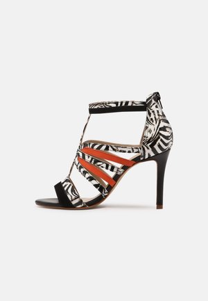 Sandał na wysokim obcasie wykonany z czarno-białej tkaniny w paski zebry, z pomarańczowymi paskami akcentowymi i smukłą sylwetką oraz otwartym przodem.