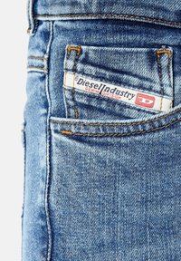 Ljusblå denimjeans med en bakficka som har en vit etikett med texten "Diesel Industry Denim Division" och röda detaljer.