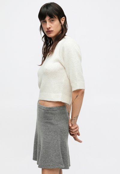 Przycięty biały sweter z dzianiny z krótkimi rękawami, zestawiony z szarą rozkloszowaną spódnicą. Sweter ma miękkie, teksturowane wykończenie.