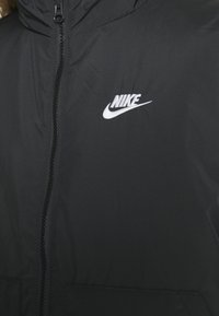 Nike crna dukserica s kapuljačom koja ima cijeli zip, mekanu teksturu i bijeli logo na lijevoj strani prsnog područja.
