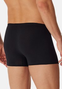 Boxer-briefs noirs avec une texture lisse, une taille élastique et un design à jambes courtes, mettant en avant un ajustement snug et un style simple.