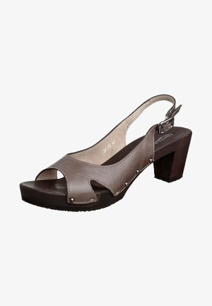 Sandalia marrón de cuero con abertura en los dedos, tira trasera con hebilla, tacón grueso de madera y tachuelas metálicas decorativas en los laterales.
