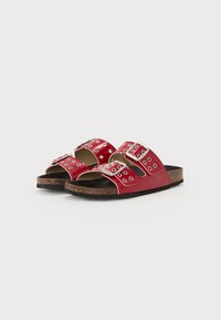 Sandales en cuir verni rouge avec deux sangles ajustables, quincaillerie en argent et semelle en liège brun texturé. Design à bout ouvert et profil plat.