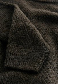 Ciemnobrązowy, dzianinowy sweter o teksturowanym wzorze. Posiada ściągacze na rękawach i miękki, puszysty wygląd.