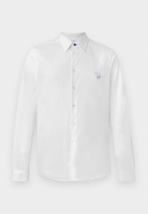 White long-sleeve shirt in smooth fabric featuring a blue button and a small embroidered design on the left side. Button-up front and collar.